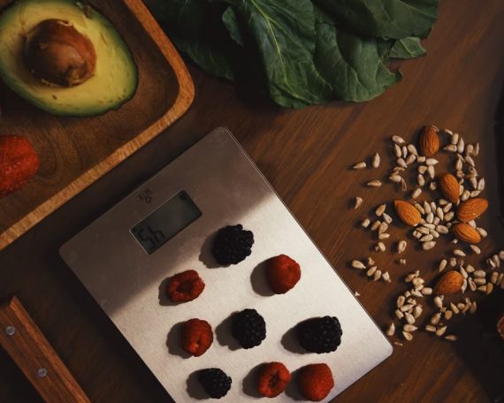 Top view of composed raw almond with seeds and avocado on table with berries on scales for cooking healthy dish